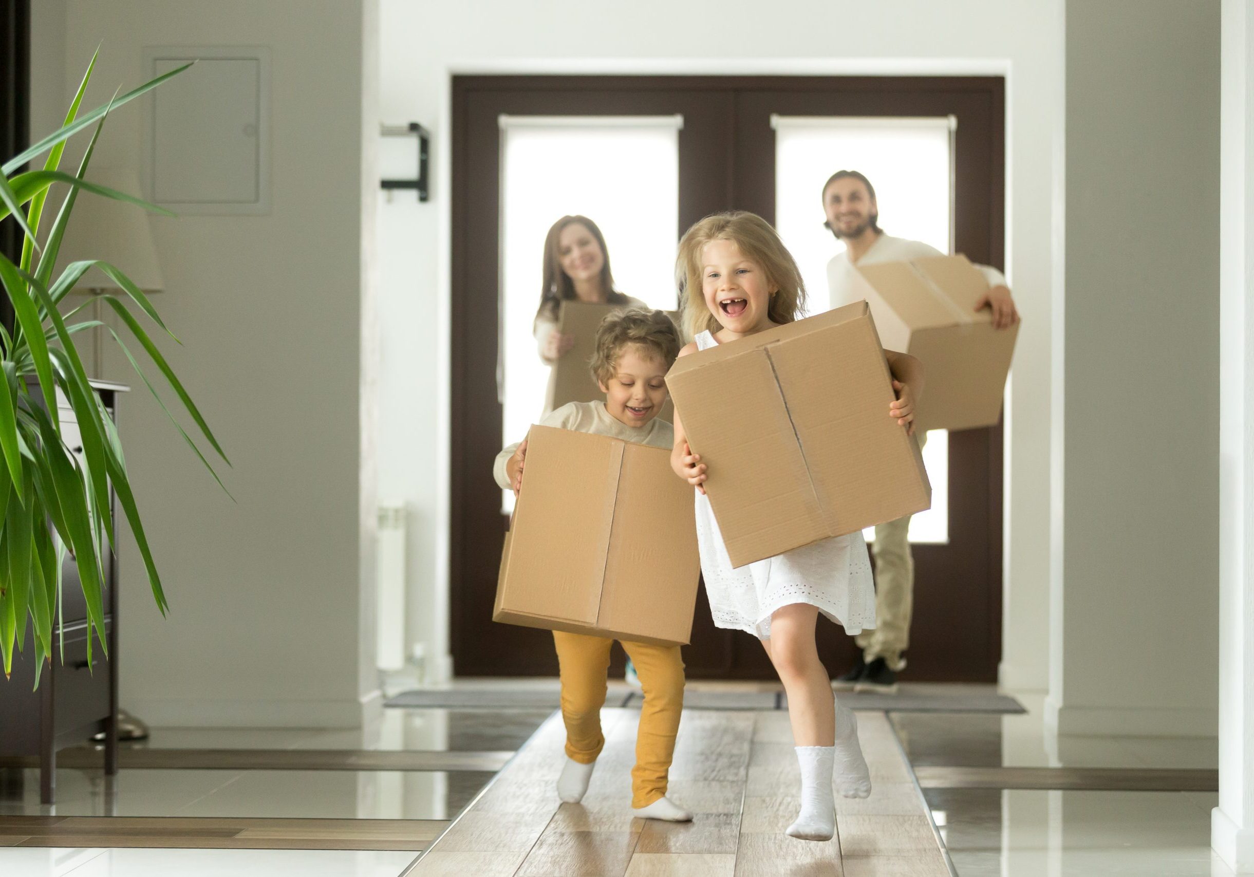 Happy family with kids bought new home, excited children funny girl and boy holding boxes running into big modern house, helping parents with belongings, moving day concept, mortgage and relocation